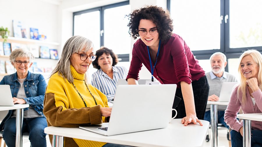 Une animatrice aide des seniors à utiliser un ordinateur portable